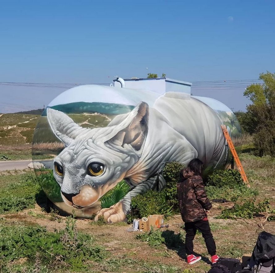Un artiste de rue peint une illusion bluffante d’un chat sphynx sur un vieux réservoir d’essence